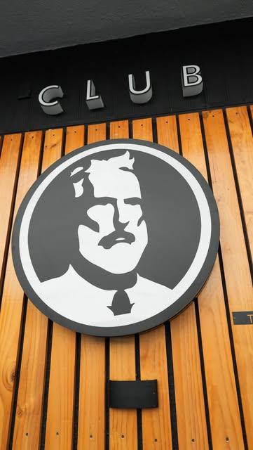 El logo de Chevalier Club, el caballero de bigote, montado en una pared de listones de madera bajo la palabra CLUB