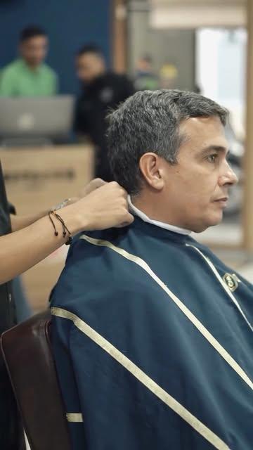 Un barbero ajusta la capa azul de rayas a un cliente de cabello canoso antes del corte
